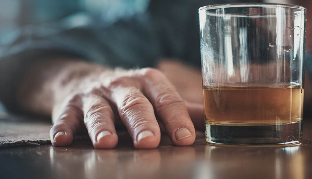 Hand by glass of liquor, man's head on table